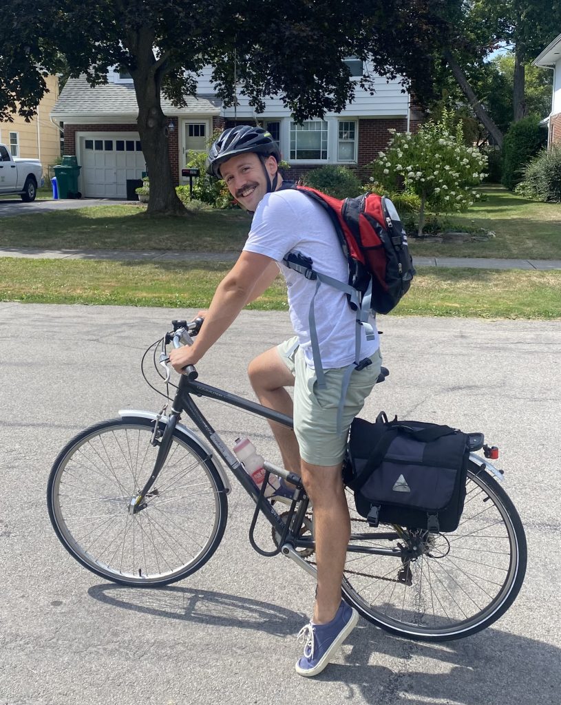 Chaz Goodman (guest blogger) smiling on his bike. He's wearing a black helmet and red backpack.