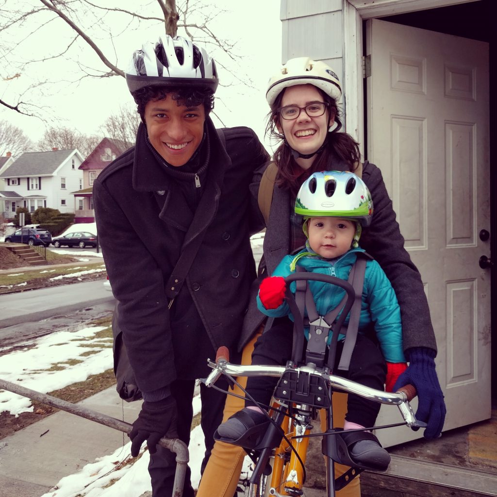 Two parents with their child; one parent is on a bike with the child; all wearing helmets