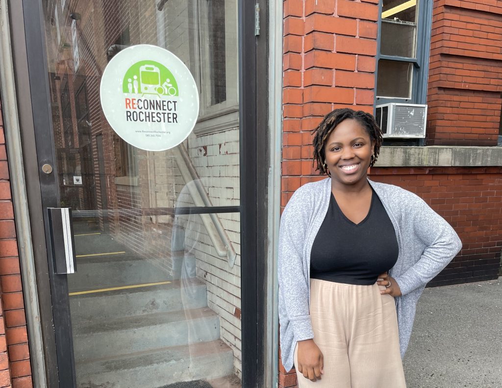 Jahasia Cooper-Esgdaille stands outside the Reconnect Rochester office door, smiling!