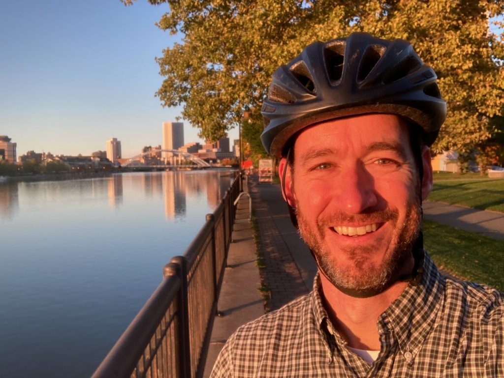 Doug Kelly smiles in a helmet next to the Genesee River