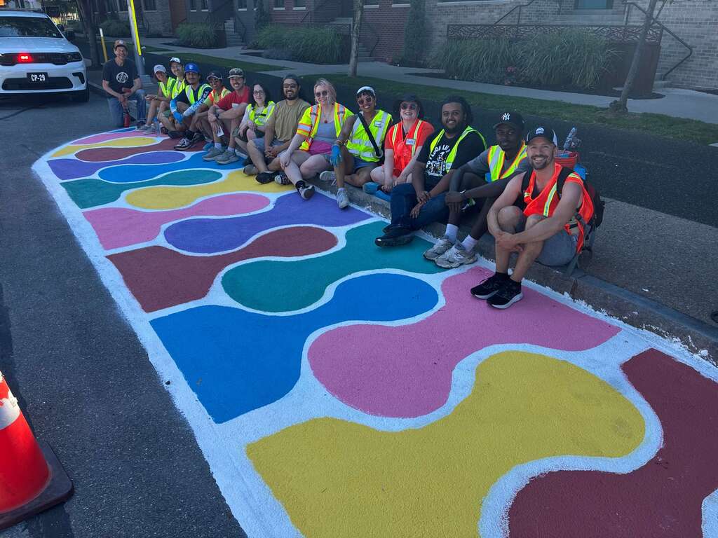 IMG_0269 (1) (1) a group of people smiling sitting on a curb in front of a brightly colored mural